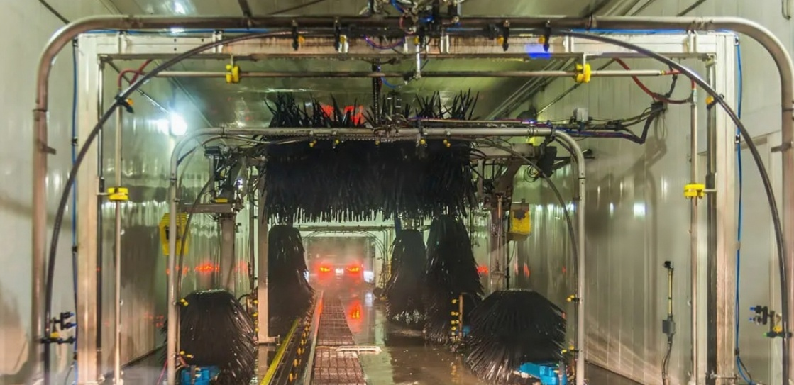 Carro passando por um túnel de lavagem automática com jatos de água e escovas giratórias.